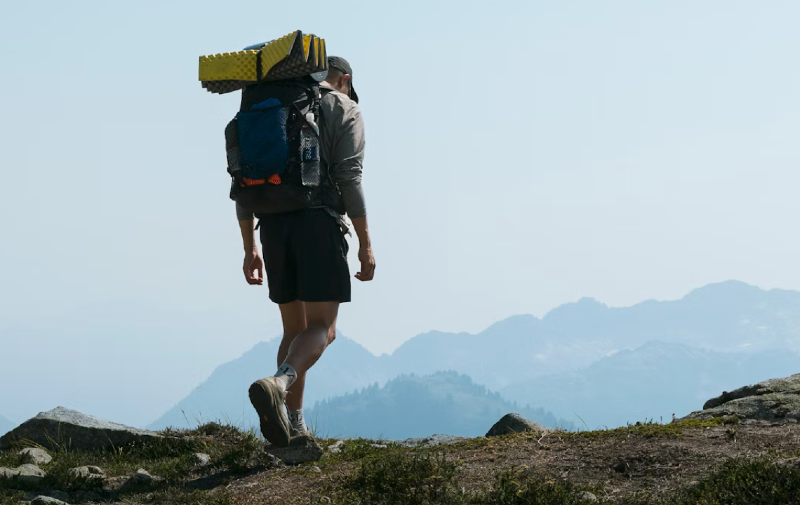 Backpacker hiking on a mountain trail carrying an ultralight backpack with a sleeping pad and gear.