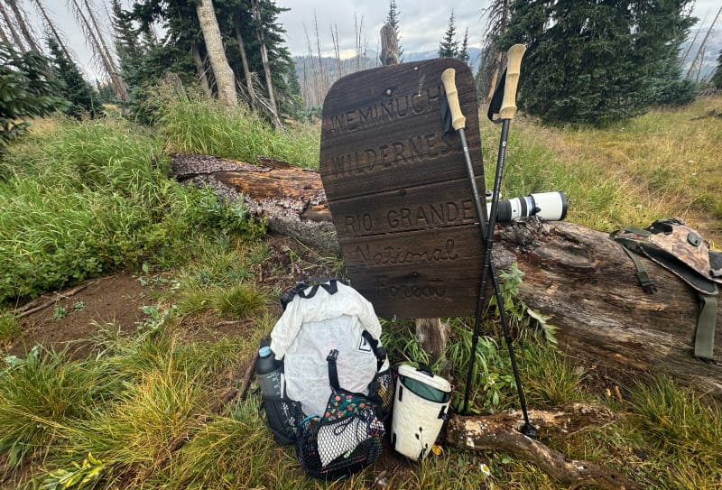 Ultralight Gossamer Gear trekking poles and backpack leaning against the Weminuche Wilderness sign in Rio Grande National Forest, Colorado.
