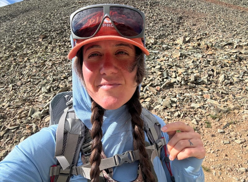 Hiker wearing HIMALI Eclipse Sun Hoodie with hood up and backpack, demonstrating its sun protection and layering compatibility.