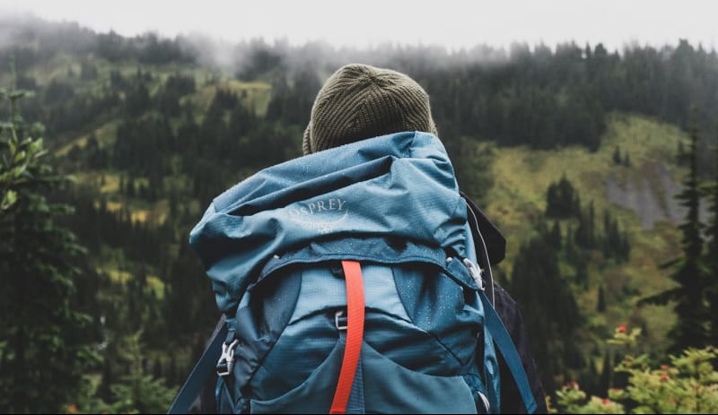 Hiker wearing an Osprey backpack facing misty mountain scenery.