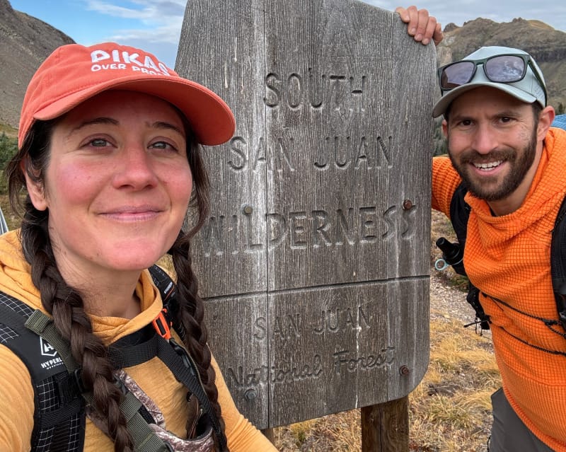 Two hikers at the South San Juan Wilderness sign, one carrying the Hyperlite Windrider 70 Backpack loaded for a multi-day trek.