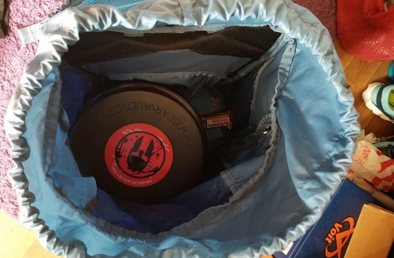 Open hiking backpack with a bear canister and gear packed inside.