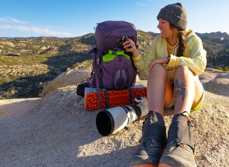 Backpacker sitting on a rock with an Osprey pack, camera gear, and trekking essentials.