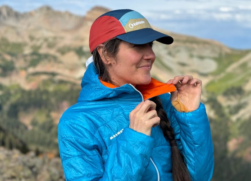 Close-up of a hiker adjusting the collar of the Mammut Eigerjoch Light IN Hooded Jacket while standing in the mountains.