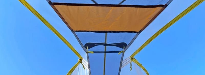 Inside view of a mesh-lined tent ceiling with a blue sky above.