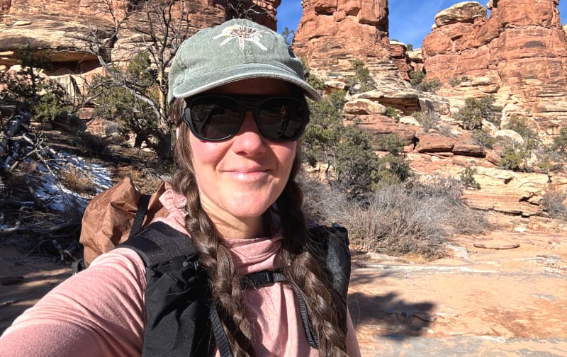 Hiker wearing Ombraz sunglasses on a red rock desert trail with sandstone formations in the background.