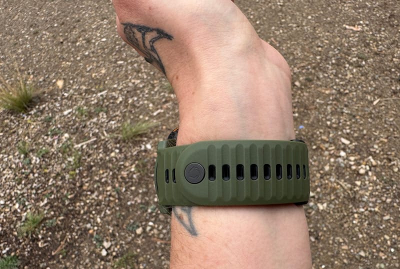 Close-up of the green COROS Nomad Watch strap with logo detail, shown on wrist against a dirt trail background.