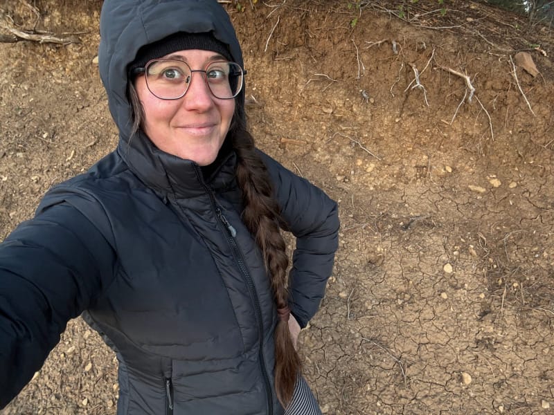 Hiker wearing the black KUIU Elements Hooded Jacket with hood up outdoors, demonstrating fit and coverage during cold-weather testing.