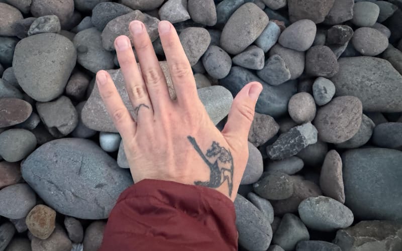 Hand wearing PAKA Mayu Ultralight Jacket sleeve resting on river rocks outdoors.
