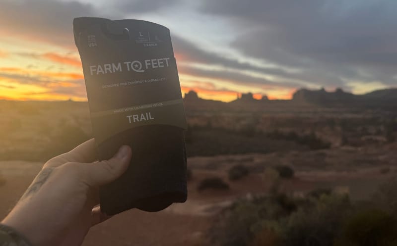 Farm To Feet Trail merino wool socks held up against a colorful desert sunrise landscape.