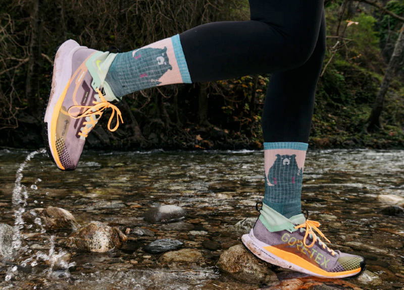 Trail runner crossing a creek wearing colorful Darn Tough hiking socks and Gore-Tex shoes.