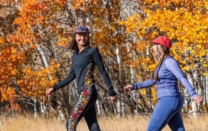 Three women hiking through a forest of bright orange fall trees wearing Wild Rye Bassett baselayers.