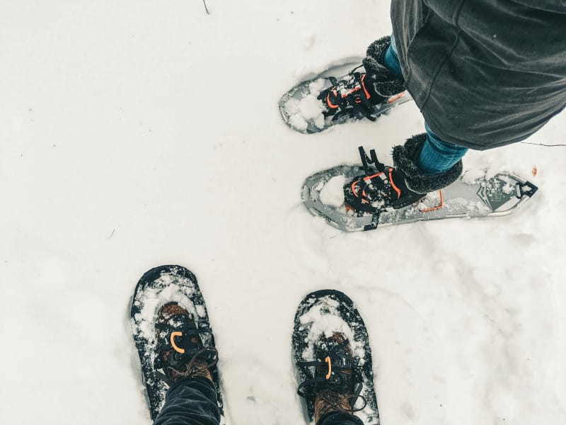 Top-down view of two people wearing snowshoes while standing on a snowy trail, showing how snowshoes distribute weight for easy winter hiking.