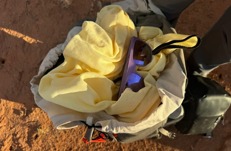 FarPointe Sun Cruiser stuffed into an open backpack with sunglasses, showing its lightweight and packable design.