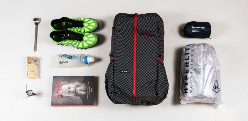 Ultralight backpacking gear flat lay including pack, trail running shoes, tent, sleeping pad, water filter, and stove