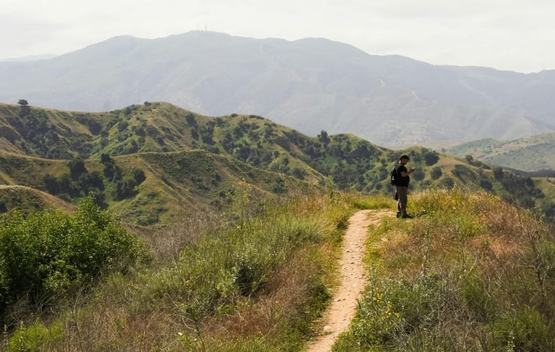 Hiker standing on a narrow dirt trail through rolling green hills during a lightweight hiking trip