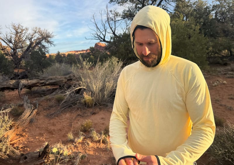 Man wearing the FarPointe Sun Cruiser with the hood up, standing in desert terrain during golden hour.