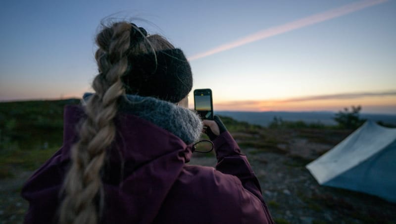 Backpacker at camp taking a photo at sunset beside an ultralight tent in the mountains
