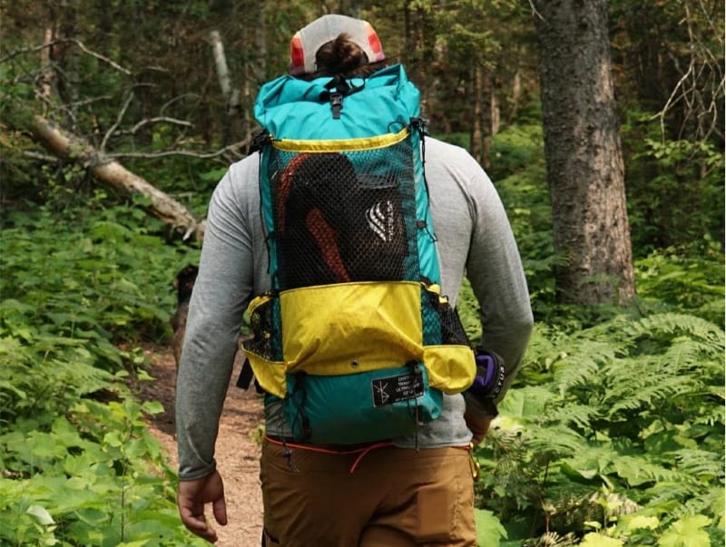 Hiker wearing a Chicken Tramper Ultralight Gear backpack on a forest trail, showing mesh pockets and lightweight pack design.