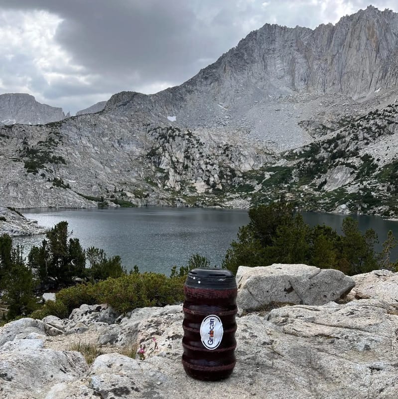 Grubcan Wave bear canister placed near an alpine lake during a backpacking trip in bear country