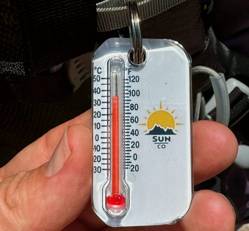 Close-up of thermometer showing high temperatures during a hot desert hike, emphasizing heat exposure and hydration needs
