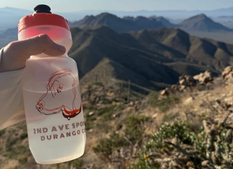 Electrolyte drink bottle held on a desert mountain ridgeline during a hot hike in the Southwest