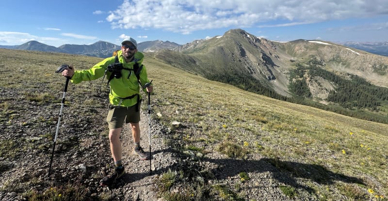 Photographer hiking with trekking poles while wearing HIMALI outerwear in an alpine mountain environment