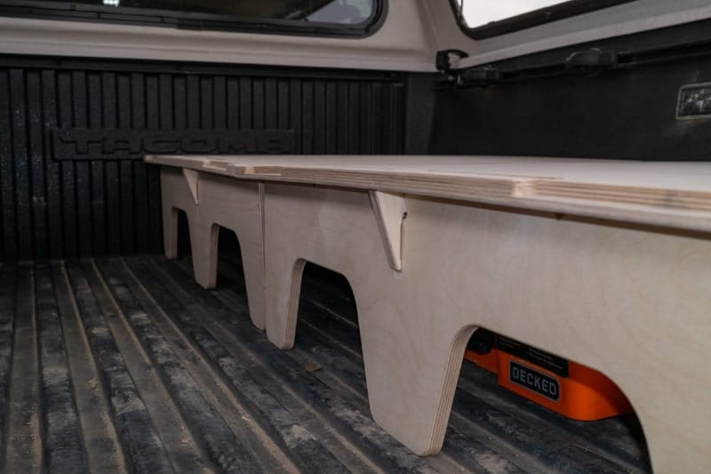 Side view of BamBeds Solo Full sleeping platform installed in Toyota Tacoma truck bed showing wood frame and storage underneath.