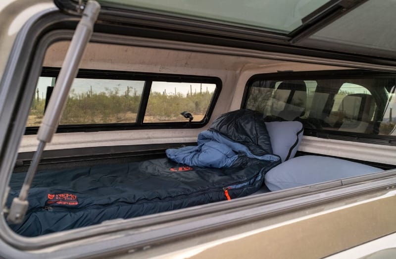 BamBeds truck bed sleeping platform inside Toyota Tacoma camper shell with sleeping bag and pillow set up for truck camping.