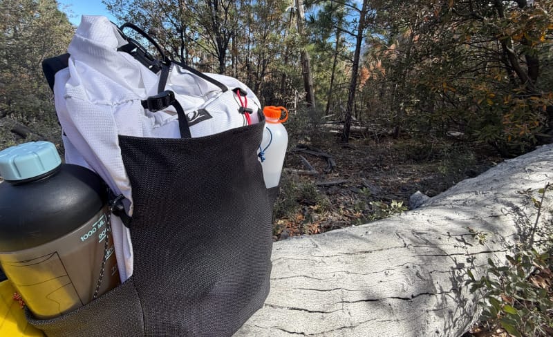 Outdoor Vitals Skyline 30 Fastpack loaded with gear in forest setting, showing large rear mesh pocket with water bottle and extra storage.