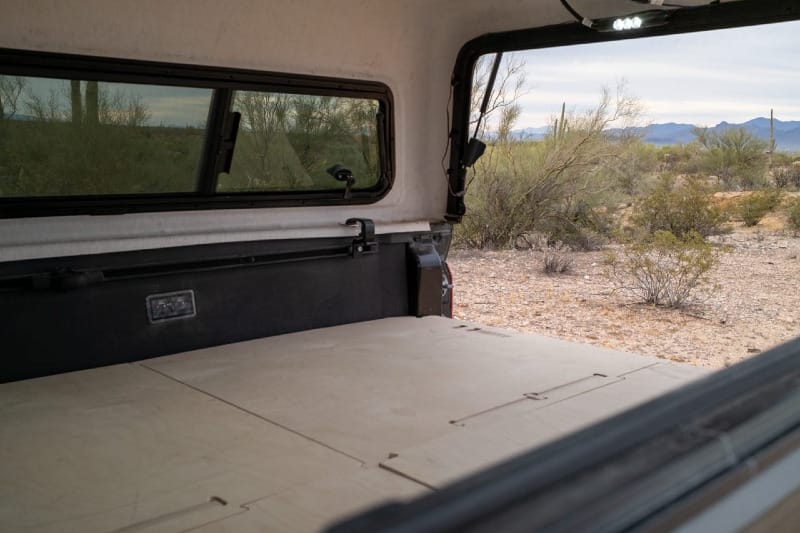 Interior view of BamBeds full sleeping platform inside Tacoma truck topper with flat wood sleeping deck ready for camping.
