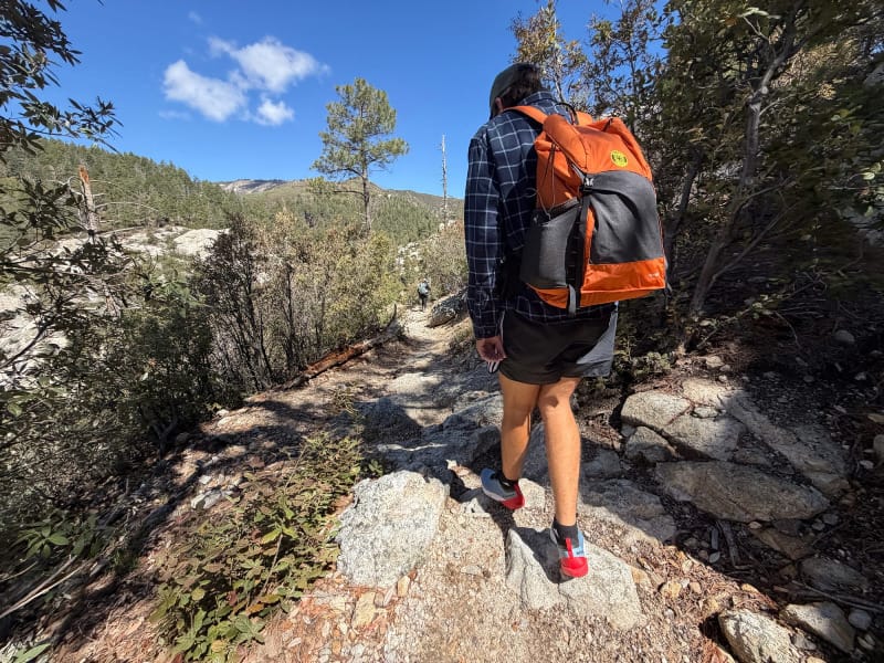 Hiker wearing Mammut Aenergy Trail Speed shoes descending a rocky mountain trail with a backpack.