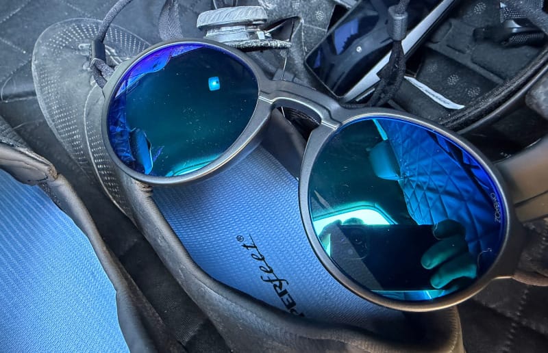 Close-up of Ombraz Blue Mirror sunglasses resting on cycling gear with reflective blue mirrored lenses visible.