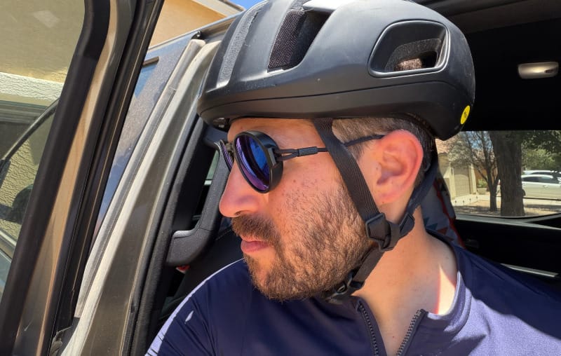 Cyclist wearing Ombraz Blue Mirror sunglasses and a black cycling helmet beside a vehicle in sunny Arizona conditions.