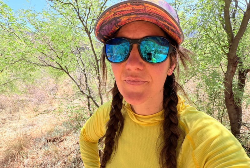 Woman hiking in the Sonoran Desert wearing Ombraz Blue Mirror sunglasses and a yellow sun hoodie.