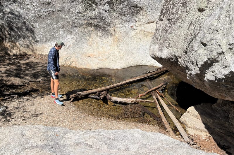 Hiker wearing Mammut Aenergy Trail Speed shoes standing beside a rocky mountain creek and granite boulders.