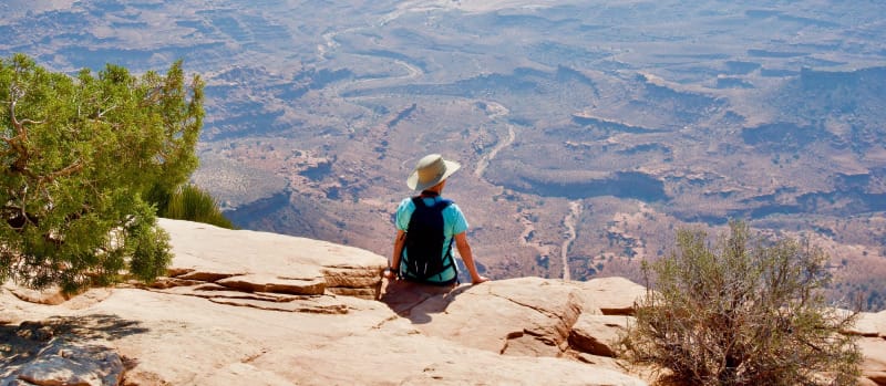 Hiker sitting on a canyon overlook in the desert, reflecting on adventures while wearing the best trail runners and hiking shoes for backpacking and desert hiking in 2026.