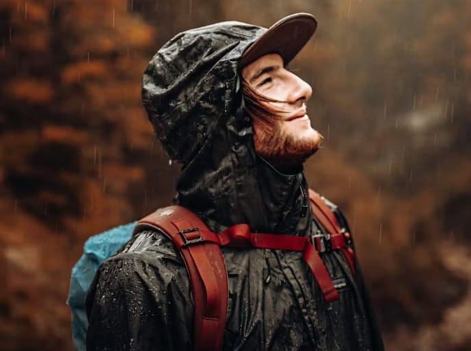 Hiker wearing a hooded waterproof rain jacket and backpack while hiking in heavy rain.
