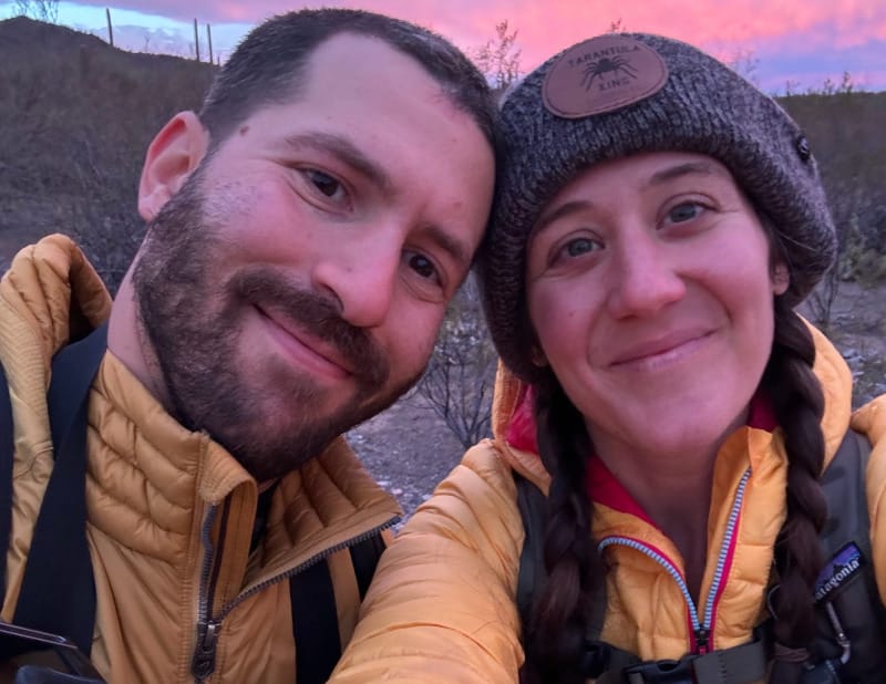 Two hikers wearing insulated puffy jackets on a desert trail at sunset, illustrating synthetic and down hiking insulation.