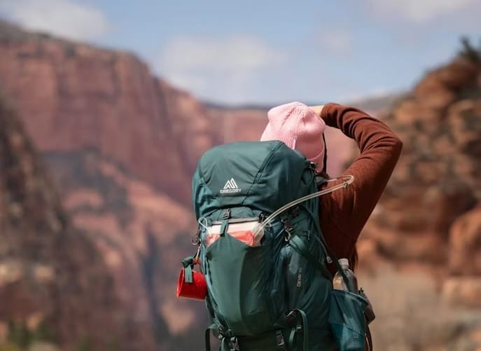 Hiker wearing a lightweight jacket and carrying a large backpack on a desert canyon trail.