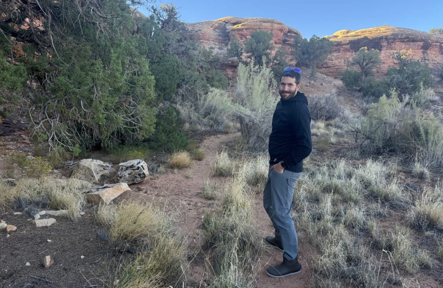 Hiker wearing a black fleece hoodie on a desert trail surrounded by red rock and high-desert vegetation.