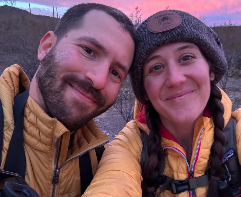 Two hikers wearing lightweight yellow down jackets and backpacks during a colorful sunset hike.