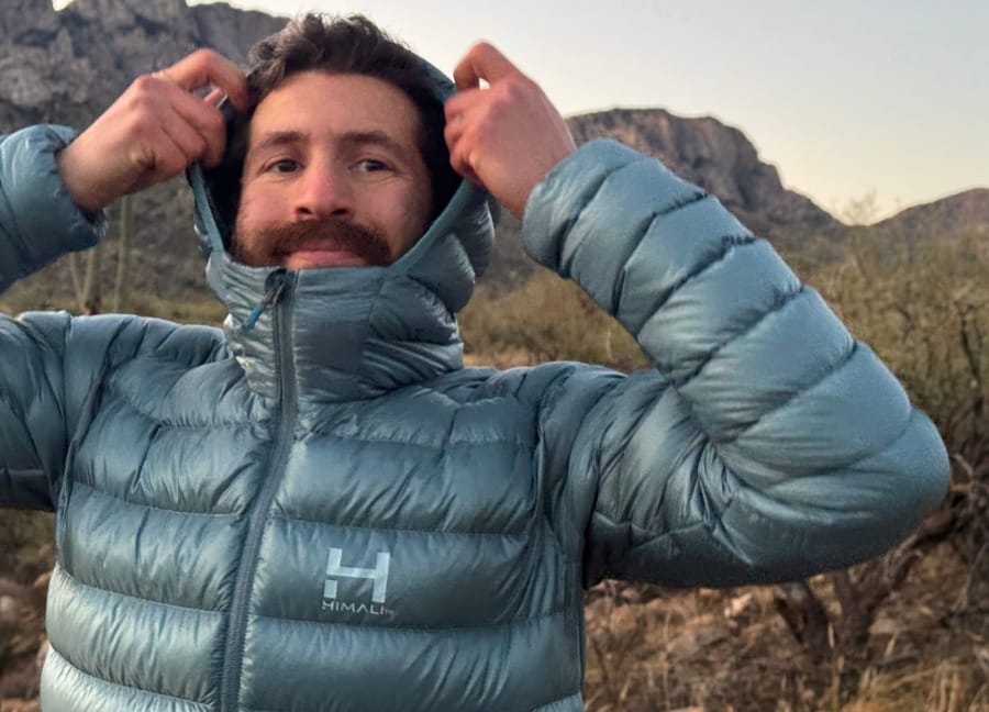 Hiker wearing a lightweight blue hooded down jacket in rocky mountain terrain.