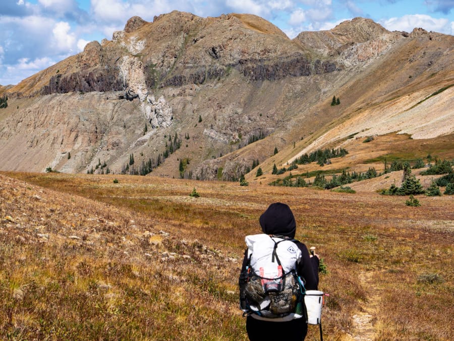 Backpacker carrying an ultralight Hyperlite Mountain Gear pack while hiking through alpine terrain in autumn.
