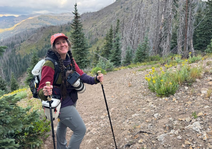 Hiker and wildlife photographer wearing KUIU pants and technical layers on a mountain trail.