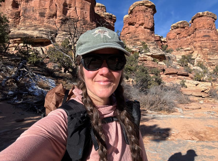 Hiker wearing a pink PAKA alpaca wool hoodie on a desert hiking trail among red rock formations.