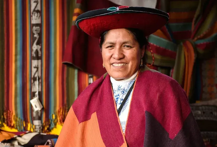 Peruvian artisan wearing traditional clothing in front of colorful woven textiles as PAKA celebrates its 10th anniversary.