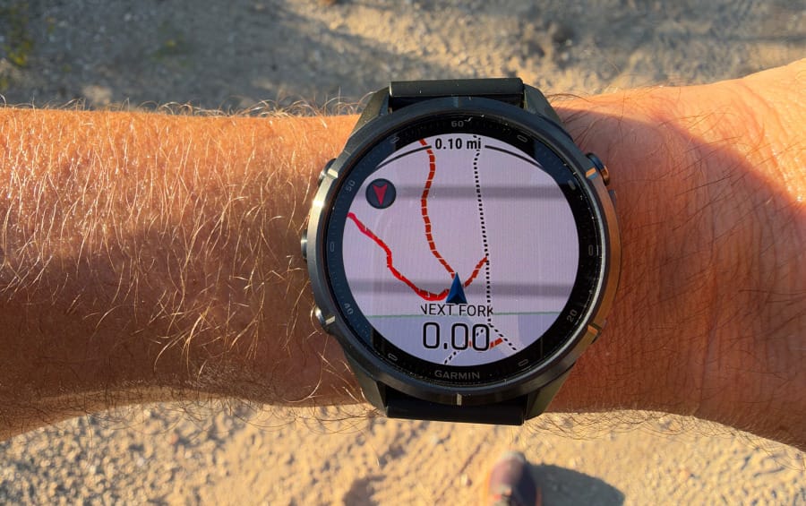 Side view of a Garmin fēnix 9 Pro inReach GPS watch worn on a hiker's wrist, showing its thick case, side buttons, and black silicone strap.