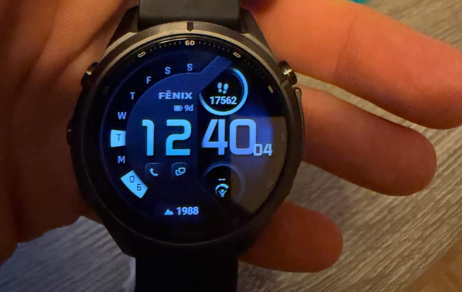 Close-up photograph of a Garmin fēnix 9 Pro inReach smartwatch displaying the time, step count, battery estimate, and elevation on its digital watch face.