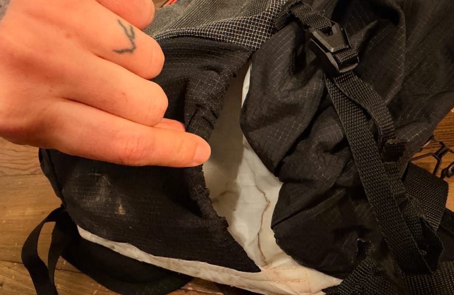 Close-up of a hand examining the black mesh pocket, stitching, and adjustable buckle on the Hyperlite Aero 28 ultralight backpack.